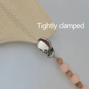 Silicone beads and wooden pacifier clip shown tightly clamped on textured fabric