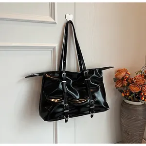Close-up of black glossy patent leather tote bag with silver buckles and vertical straps