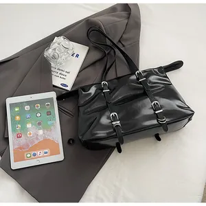 Close-up of black glossy leather tote bag with silver metal buckles on a grey suit jacket