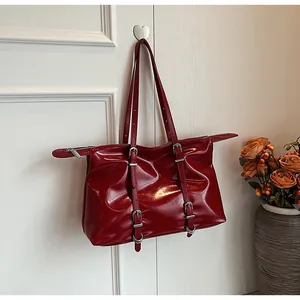 Detail of red glossy patent leather tote bag hanging on a white decorative wall hook