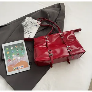 Detailed top view of a glossy red tote bag with silver buckles on a gray blazer