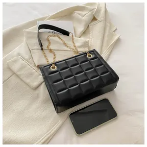 Detalle de bolso acolchado negro con cadena dorada junto a un teléfono móvil pequeño