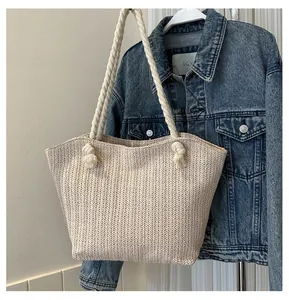 Close-up of beige woven straw tote bag featuring thick cotton rope handles and knot details