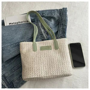 Flat lay of a woven straw tote bag with green leather handles and brand lettering detail