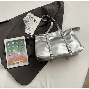 Close-up of metallic silver tote bag with buckle details on grey blazer background