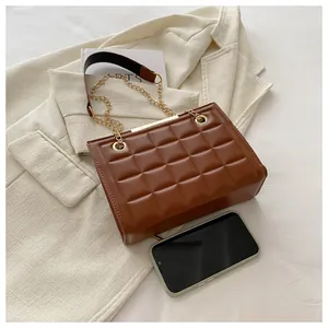 Detalle de bolso acolchado marrón con cadena dorada sobre una chaqueta blanca