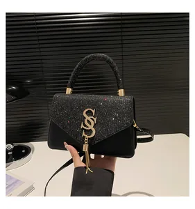 Détail d'un sac à main noir pailleté avec logo SS en métal doré et pompons élégants