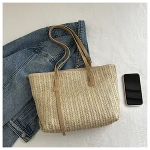 Detail of woven straw tote bag with brown faux leather straps and decorative ribbons