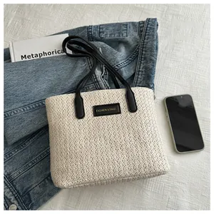 Detail shot of a beige woven tote bag with a black leather fashion label and leather straps