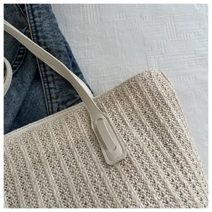 Close-up of beige woven straw tote bag featuring premium leather handles and stitching