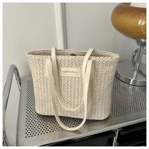 Detail of woven straw tote bag featuring leather logo patch and metal magnetic closure