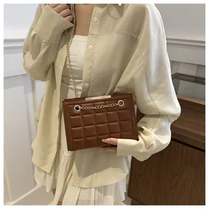 Detalle de bolso bandolera marrón acolchado con cadena dorada metálica en una modelo