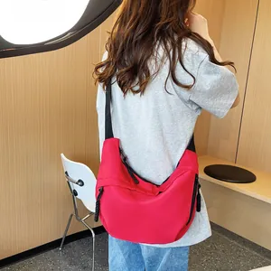 Red nylon crossbody crescent bag with wide black strap shown in stylish outdoor use