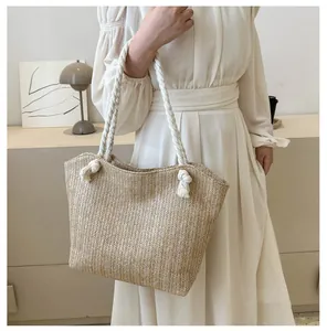 Detail of woven straw tote bag featuring thick white cotton rope handles and knot accents