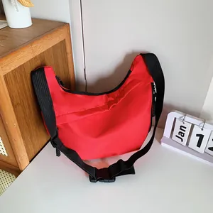 Detailed close-up of a red crescent nylon crossbody bag with black adjustable strap and zipper