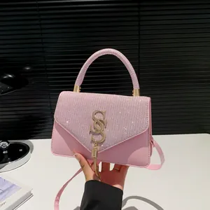 Sac à bandoulière rose pailleté avec logo SS doré et pompon sur un bureau blanc