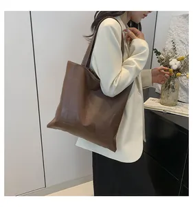 Brown leather tote bag featuring a minimalist grid pattern worn by a model in a white suit