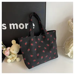 Détail de la texture d'un sac cabas en velours noir avec des motifs de fraises rouges