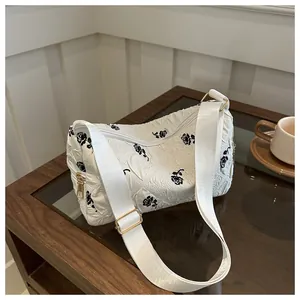 Detail of white quilted floral shoulder bag with black rose embroidery on a wooden table
