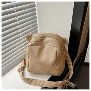Dettaglio di una borsa a tracolla in tela beige con cerniere argento e logo rosso