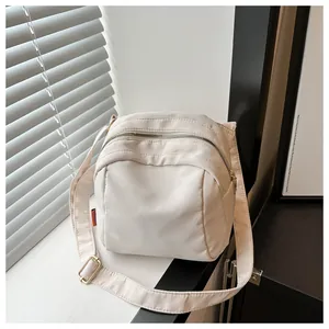 Vista dettagliata della borsa beige a tracolla con cerniera curva e etichetta