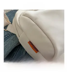 Dettaglio della borsa cilindrica bianca con etichetta arancione e zip in metallo lucido