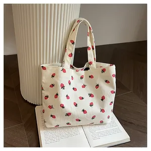Détail d'un sac fourre-tout en velours crème à motif fraise posé sur un livre ouvert
