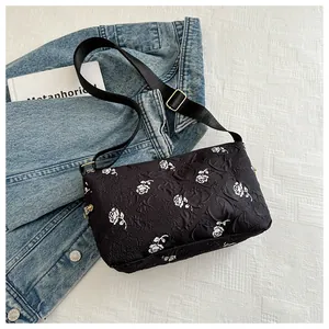 Detailed view of black floral shoulder bag with textured fabric and white rose pattern
