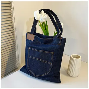 Detail of blue denim tote bag with orange contrast stitching and leather patch texture