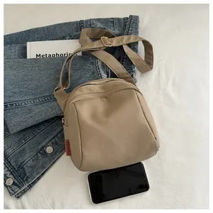 Dettaglio borsa a tracolla in nylon kaki con etichetta fashion su tessuto bianco