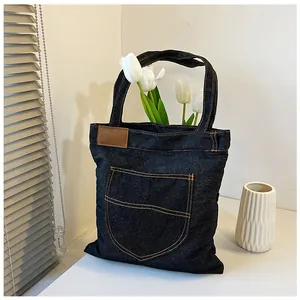 Detail of dark blue denim tote bag with orange stitching and brown leather patch