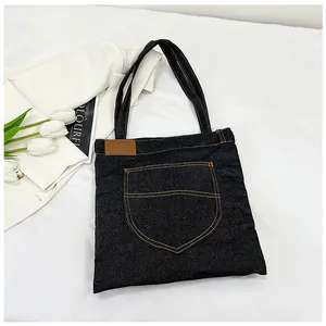 Close-up of black denim tote bag featuring vintage pocket detail and brown leather tag