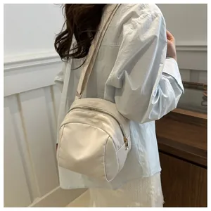 Dettaglio della borsa a tracolla in nylon crema con cerniere dorate e tracolla regolabile