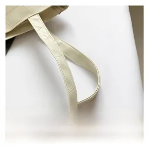 Detail of a creamy white tote bag showing a comfortable wide strap with fine pebble texture