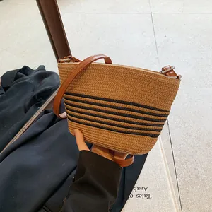 Close-up of woven straw crossbody bucket bag with dark stripes and leather strap