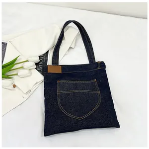 Detailed view of dark blue denim tote bag with pocket and brown leather patch