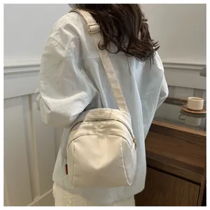 Borsa a tracolla minimalista in nylon bianco indossata da una modella in un caffè
