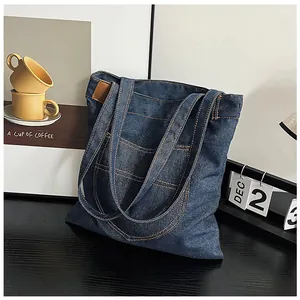 Detail of dark blue denim tote bag with yellow contrast stitching and leather tag accent