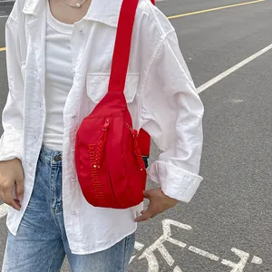 Detail of red nylon crossbody bag with embroidery and dual zipper on white shirt