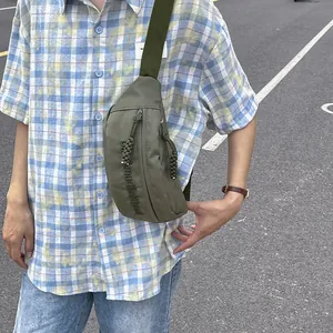 Detail of olive green nylon sling bag featuring wide shoulder strap and woven zipper pull