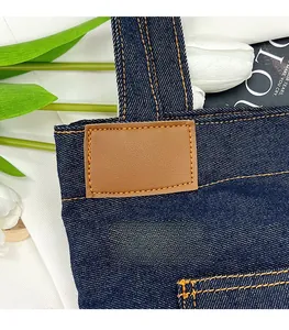 Close-up of blue denim tote bag featuring orange stitching and brown PU leather patch