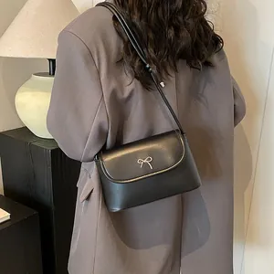 Detailansicht der mattschwarzen Umhängetasche mit silberner Schleife auf grauem Blazer