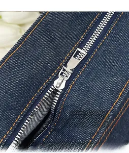 Detailed macro view of smooth silver metal zipper and orange stitching on denim tote