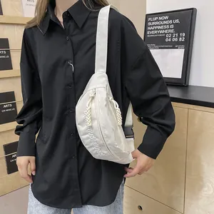 Close-up of a white nylon crossbody bag with embroidery and adjustable strap on a model