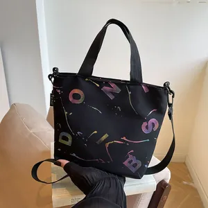 Detail of black nylon tote bag featuring gradient colorful lettering and woven handles