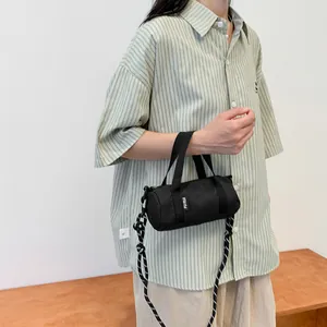 Close-up of mini black cylinder bag with striped strap and woven label on a wooden surface