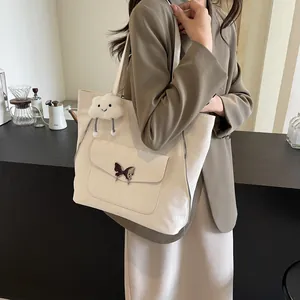 Close-up of beige tote bag with a metal butterfly clasp and a plush cloud charm