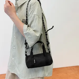 Detail of a mini black cylindrical nylon crossbody bag with a trendy woven rope strap