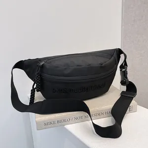 Close-up of black crossbody bag with tonal embroidery and adjustable strap on books