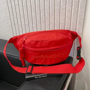 Close-up of red canvas waist bag with embroidered lettering and matching braided zipper pull